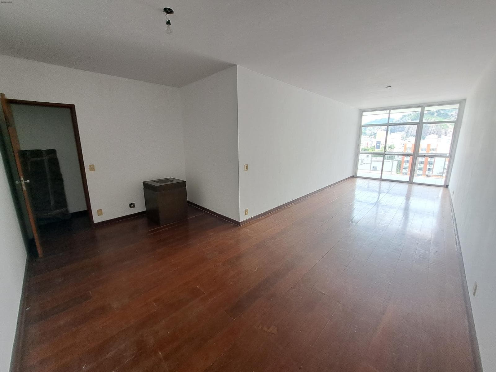 Sala espaçosa com piso de madeira, paredes brancas e grande janela com vista para o exterior