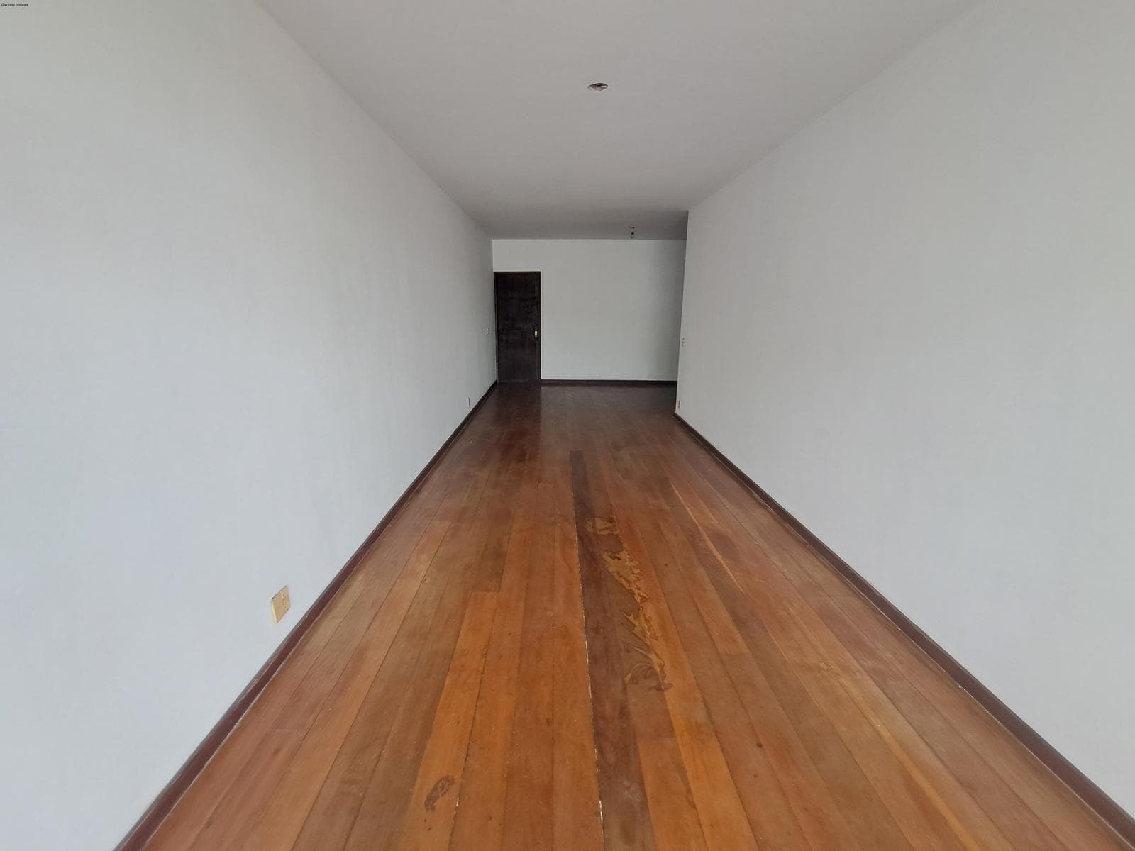 Corredor ou sala alongada com piso de madeira em tábuas corridas e paredes brancas
