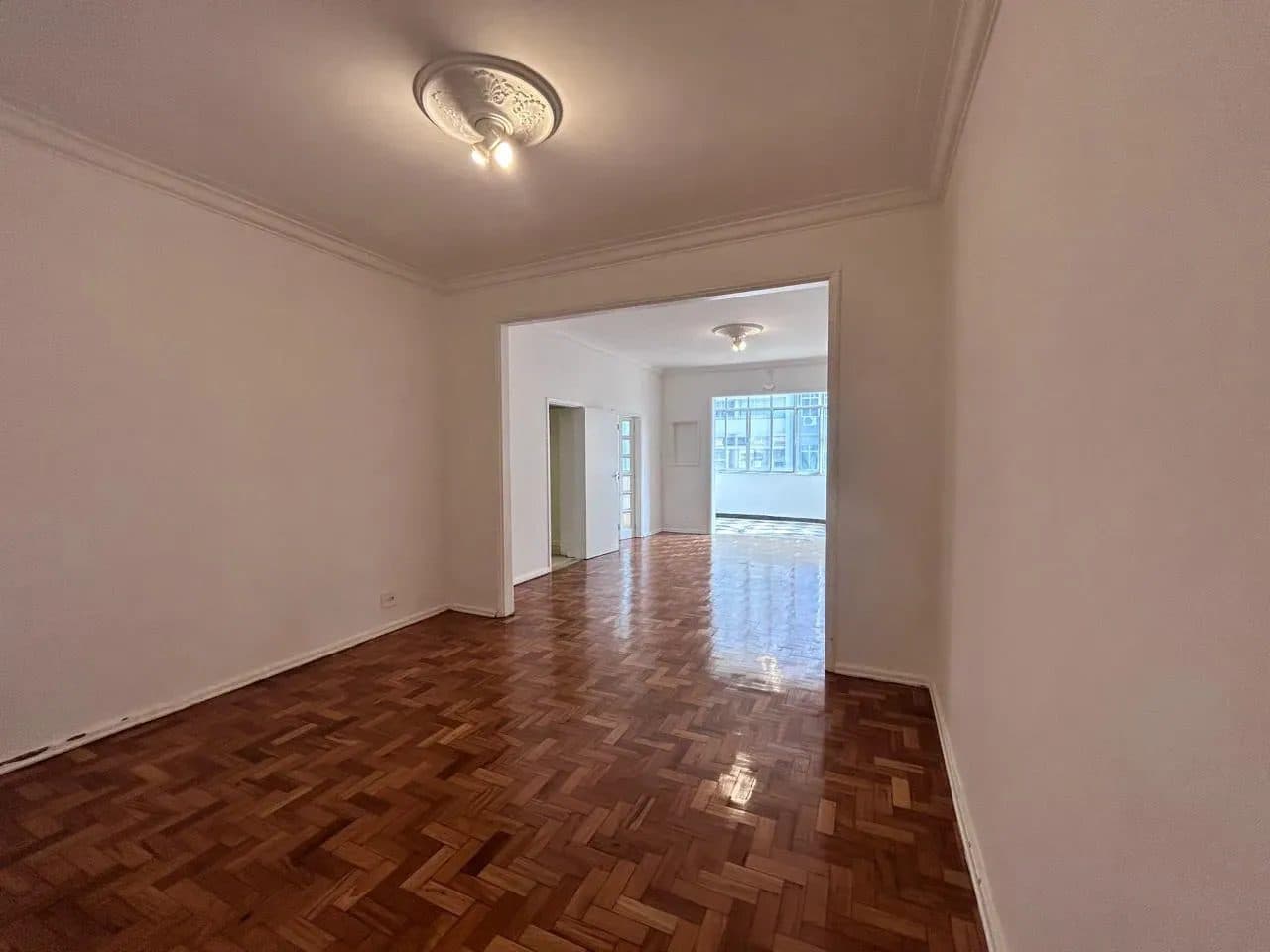 Sala ampla e vazia com piso de taco de madeira e paredes brancas.