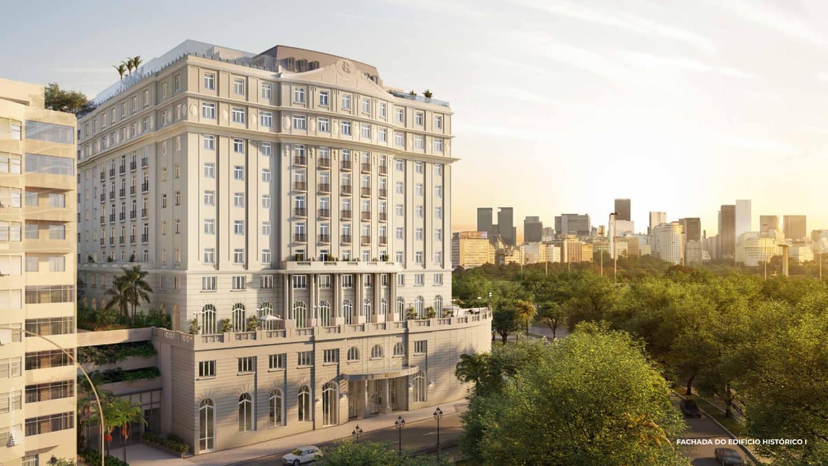 Fachada externa de edifício histórico de vários pavimentos com arquitetura clássica e vegetação ao redor.