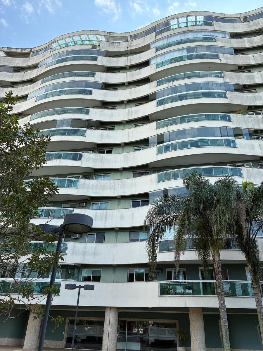Fachada do edifício residencial com varandas curvas e vegetação.