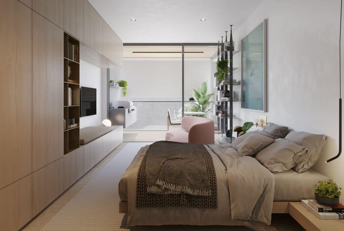 Quarto integrado com armarios planejados em tom amadeirado, cama com enxoval cinza e acesso a varanda com plantas ao fundo.