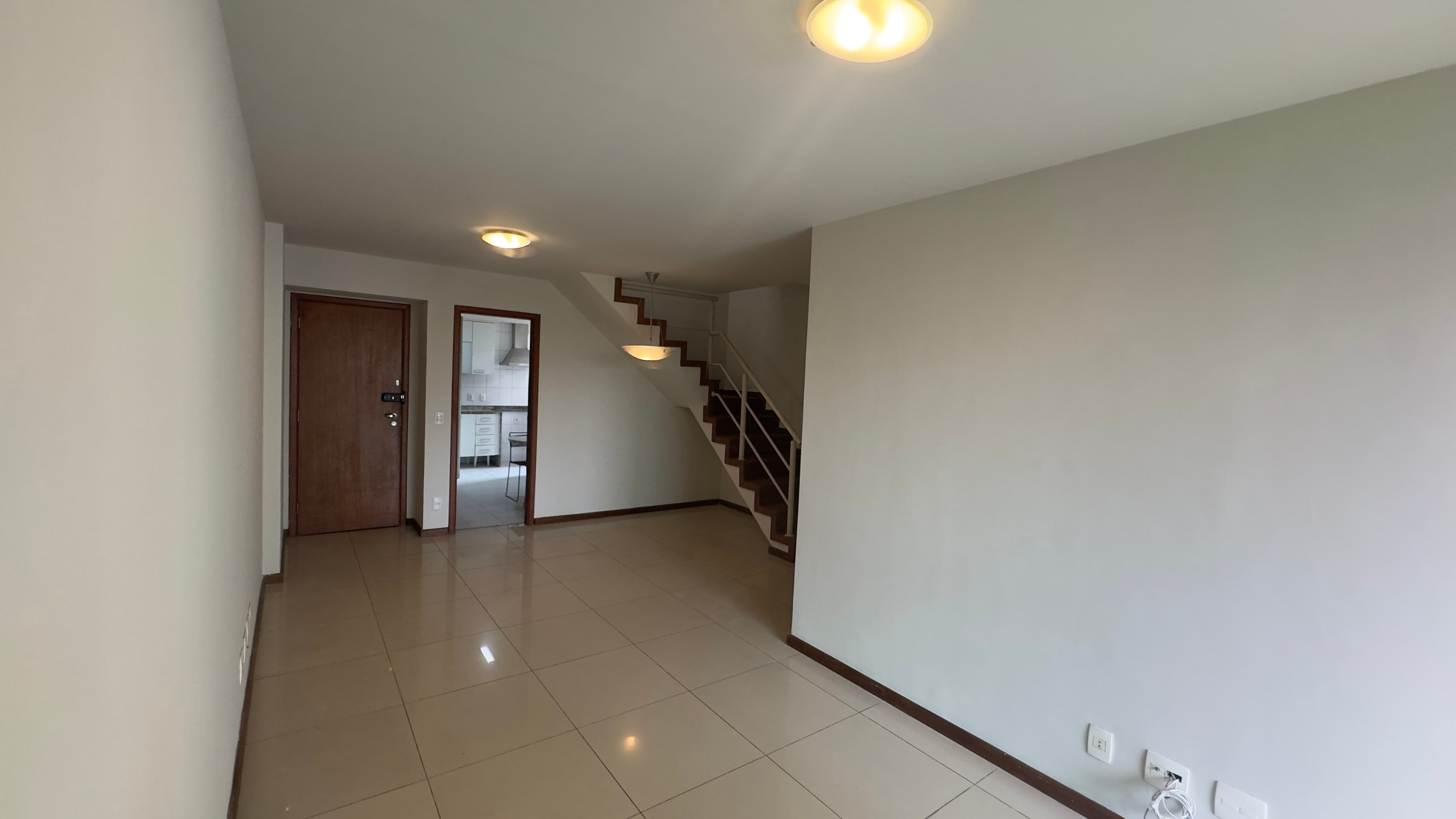 Sala ampla com piso em porcelanato claro, paredes pintadas de branco e escada de acesso ao pavimento superior.