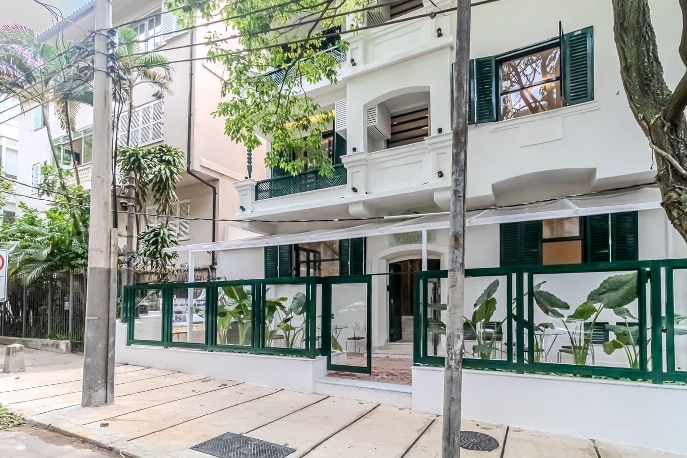 Fachada do edifício com pintura branca, janelas verdes e entrada protegida por cobertura transparente.